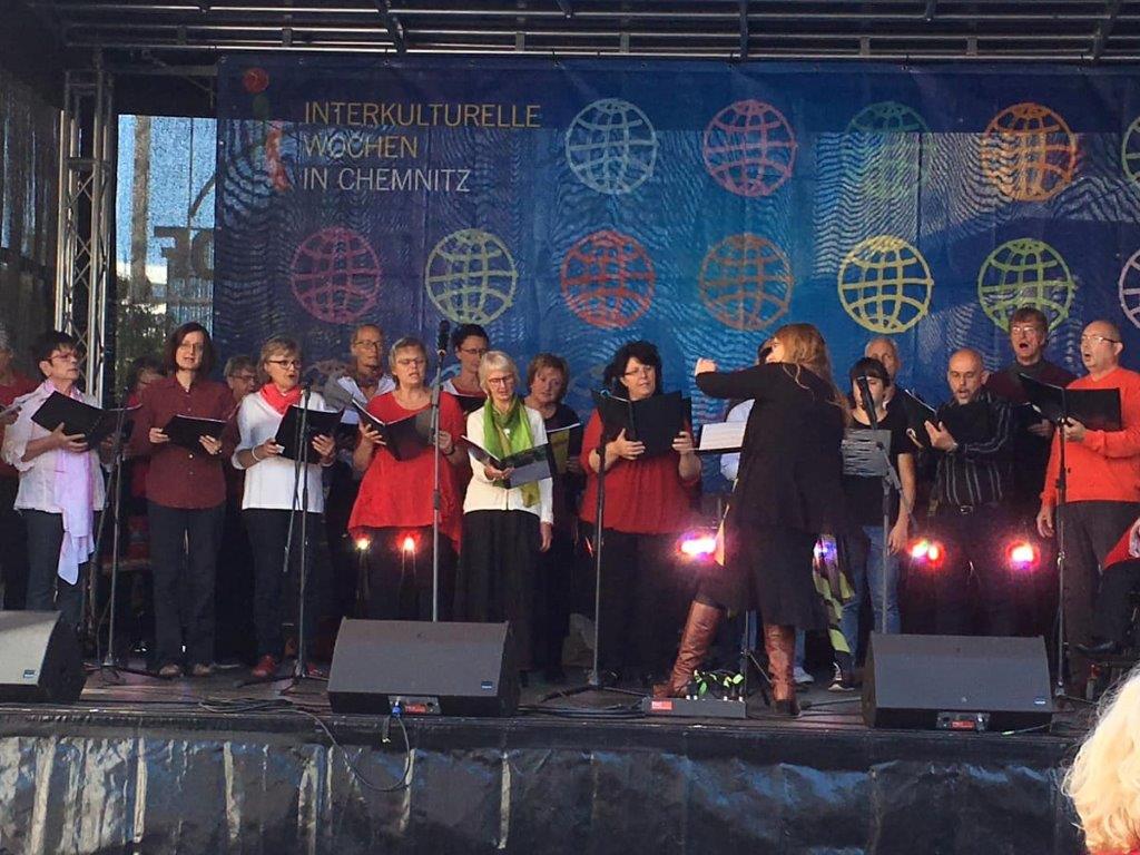 UNITY-Auftritt zu den Interkulturellen Wochen 2019 auf der Bühne auf dem Markt Chemnitz vor dem Rathaus. Chor steht bunt gekleidet auf der Bühne.