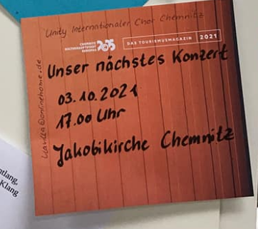 Auf einem braunen Zettel an der Pinnwand steht geschrieben: Unser nächstes Konzert 3.10.2021 17 Uhr Jakobikirche Chemnitz